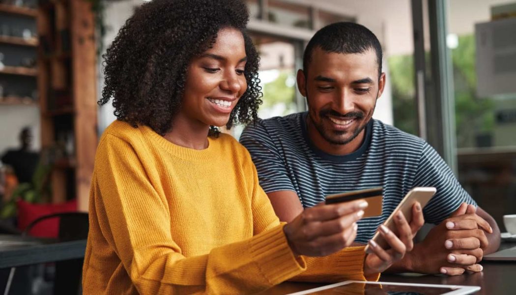 A Great Customer Experience In Action. A Man And Woman Of Color Are Shopping Online From A Coffee Shop